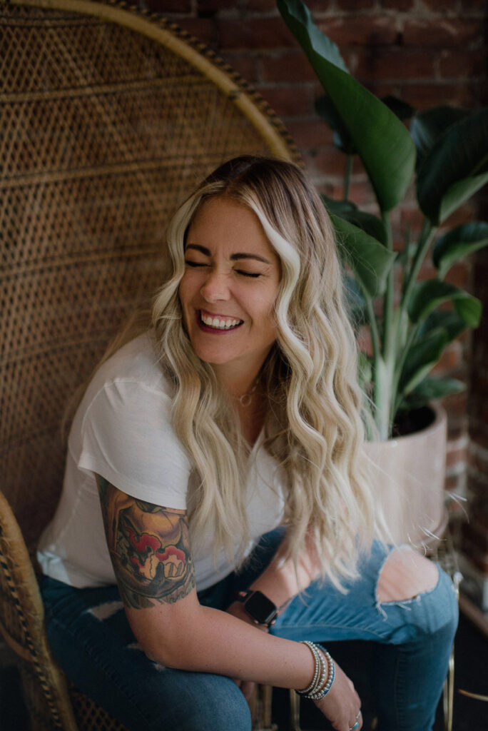 alexandra stevenson sits on a wicker high backed chair laughing as part of her signature wry humour during speaking engagements