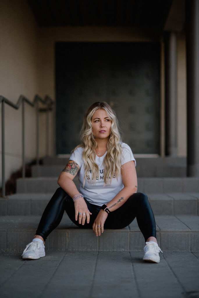 alexandra stevenson the laughing survivor sits on stone steps wearing black tights and white t that says the future is female