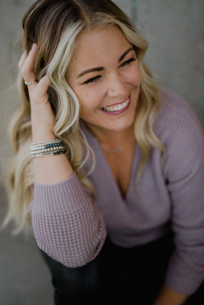 blonde hair and blue eyed alexandra stevenson laughs as she runs her hand through her hair and looks off to the right